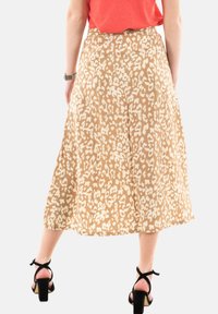 Una falda de longitud media en una tela beige con un estampado abstracto de leopardo en blanco, que presenta una cinturilla ajustada y un diseño fluido con pliegues.