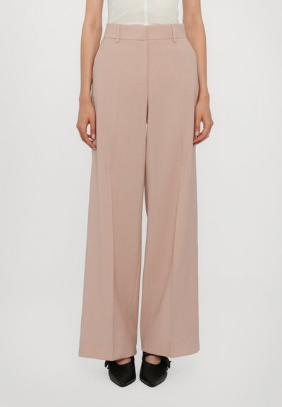 Pantaloni a gamba larga in tessuto rosa pallido, con una texture liscia e pieghe sottili. Abbinati a scarpe nere con punta affilata.