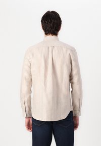 Camisa de manga larga a rayas en beige claro y crema. Presenta un cuello estándar, pliegue en la espalda y puños abotonados. El material parece suave.