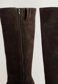 Botine de piele suede maro, de lungime până la genunchi, cu fermoar pe lateral, textură netedă și o bucată de prindere în partea de sus. Design minimalist, cu accente cusute.
