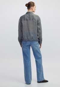 Camicia leggera e trasparente grigia a maniche lunghe con una vestibilità rilassata, abbinata a jeans di denim blu larghi. Presenta un orlo dritto e polsini con bottoni.