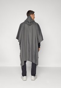 Poncho gris avec capuche, fabriqué à partir de matériaux légers. Il a une coupe ample et des fermetures ajustables sur les côtés.