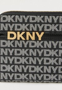 Μαύρο και άσπρο πορτοφόλι DKNY με μοτίβο, χρυσό λογότυπο DKNY και χρυσό φερμουάρ στην κορυφή.