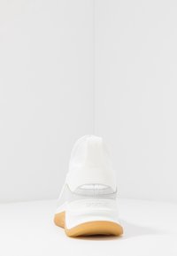 Chaussure de sport blanche avec semelle en caoutchouc, design élégant, bride élastique à l'arrière et subtils accents gris. Tige lisse avec panneau texturé.