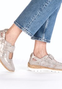 Helles graue Schuhwerk mit metallischem Glanz, featuring ein ausgeschnittenes Design und Klettverschluss. Texturierte Korksohle und weiße Gummisohle.