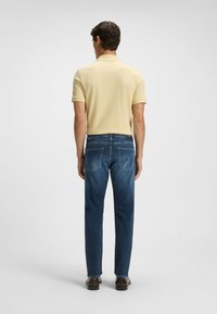 Gul kortärmad polo skjorta i kombination med mörkblå jeans. Jeansen har bakfickor och rak passform. Bruna skor kompletterar looken.