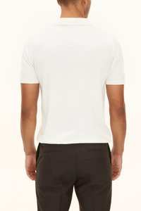 Valkoinen lyhythihainen poolopaita, jossa on klassinen kaulus, sileä pinta ja resorit hihansuissa, yhdistettynä tummiin housuihin.