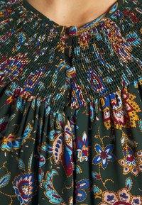 Grøn stofkjole med smocked halsudskæring, farverige blomster- og paisleymønstre samt en knaplukning med løkke-detalje.