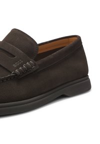 Mocassin en daim marron foncé avec détails cousus et semelle en caoutchouc, présentant un logo BOSS embossé discret sur la bride.