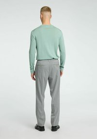 Chemise à manches longues verte clair associée à un pantalon de costume gris, avec une texture douce et deux poches arrière avec des boutons dorés. Chaussures noires.