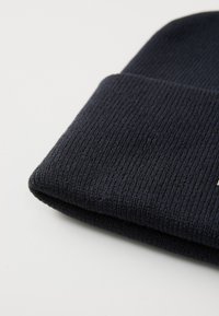 Dark navy knitted beanie with a ribbed texture, featuring a folded cuff and a minimalist logo detail on the side.
