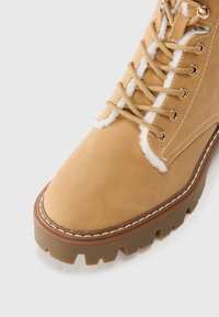 Bottine en cuir tan à lacets, présentant une doublure douce, un bout rond, des accents cousus et une semelle en caoutchouc robuste avec un motif de semelle.