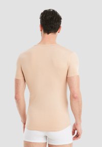 Beige short-sleeve fitted t-shirt with a round neckline and smooth texture, worn with white shorts, viewed from the back.