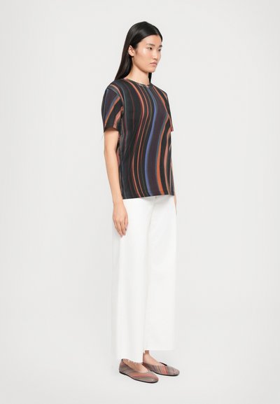 Black short-sleeve top with wavy multicolored stripes, paired with loose white pants and striped flats. Smooth fabric, relaxed fit.