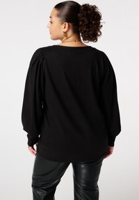 Zwarte lange mouwen top met opgezette schouders, zachte textuur en een losse pasvorm, gecombineerd met glanzende zwarte neplederen broek.