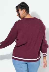 Maglione a maglia bordeaux con strisce bianche sui maniche e sull'orlo. Presenta una vestibilità rilassata e un colletto rotondo. Texture liscia, spessore medio.