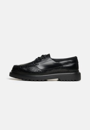 Chaussure basse en cuir noir avec texture tissée à l'avant et sur les côtés, fermeture à lacets, semelle épaisse crantée et finition lisse et brillante.