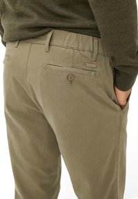 Pantaloni verde oliva in misto cotone, con chiusura a bottone, passanti per cintura e due tasche posteriori con un discreto dettaglio del logo.