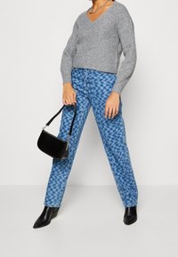 Grauer, gerippter Strickpullover mit V-Ausschnitt; blaue gemusterte Jeans; schwarze, strukturierte Handtasche; spitze schwarze Stiefeletten.