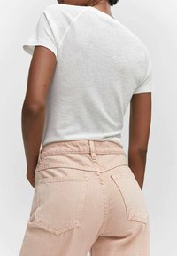 T-shirt blanc à manches courtes avec un col rond, associé à un pantalon taille haute rose clair doté de deux poches arrière et d'une texture douce.