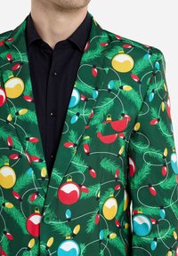 Roheline bleiser, millel on jõuluteemaline muster, kus on kaunistused ja tuled. Tal on sile tekstuur ja all on kontrastne must särk.