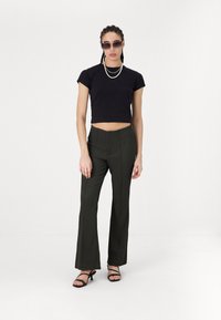 Black cropped t-shirt, high-waisted dark olive pants with vertical seams, and black strappy heels. Accessorized with sunglasses and a pearl necklace.
