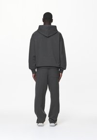 Mörkgrå huvtröja och matchande sweatpants, tillverkade av mjukt tyg, med avslappnad passform och en bakfickdetalj på byxorna.