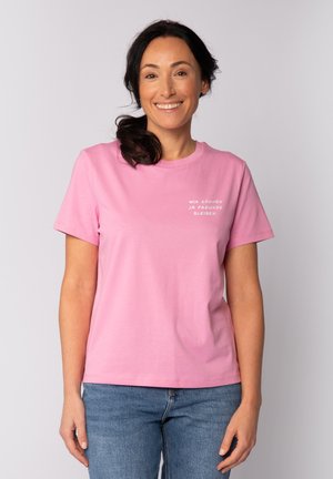 T-shirt en coton rose à manches courtes avec un texte imprimé blanc sur le devant. Design classique à col rond, porté avec un jean bleu.
