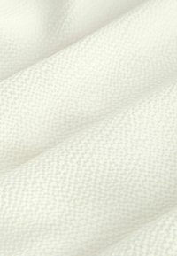 Detailný záber mäkkej bielej textúrovanej tkaniny s jemnými diagonálnymi záhybmi a jemným tkaným vzorom.