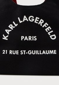 Fekete szövet fehér felirattal, amely így szól: "KARL LAGERFELD PARIS 21 RUE ST-GUILLAUME" vastag, blokks betűkkel.