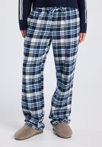 Blue and white checked flannel pajama pants with an elastic waist and drawstring. Soft texture, loose fit, paired with beige slippers.