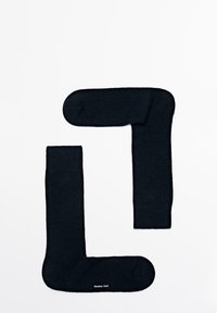 Calzini neri realizzati in un materiale morbido, con un risvolto a costine, una texture liscia e un logo stampato vicino alla punta. Disposti a forma di "L".