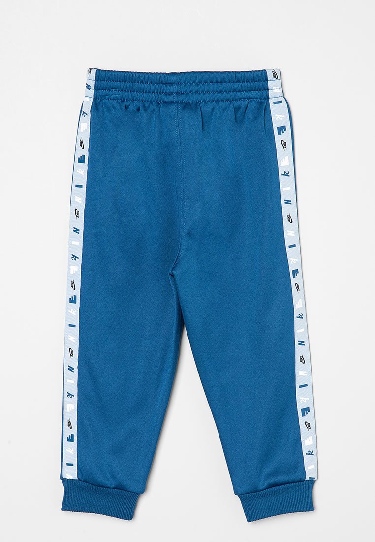 Pantalones deportivos azules con una cinturilla elástica, dobladillos ajustados y rayas laterales blancas que presentan patrones de marca y logotipos. Fabricados con un tejido suave.