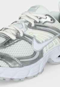 Λευκό και ασημί παπούτσι τρεξίματος Nike με επάνω μέρος από δίχτυ, κλείσιμο με κορδόνια και παχιά υφή στην σόλα, ορατό από μπροστινή πλευρική γωνία.