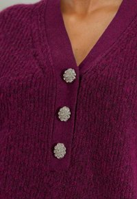 Cárdigan de punto color ciruela con escote en V y tres botones metálicos en forma de flor con detalles transparentes en la parte delantera.