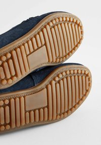 Granatowe zamszowe buty z teksturowanymi gumowymi podeszwami, z rzędami rowków i okrągłych kropek zapewniających przyczepność i grip.