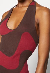 Stricktanktop mit tiefem Ausschnitt; verfügt über wellenförmige Muster in Weinrot und Braun. Weicher Stoff, ärmelloses Design und figurbetonte Passform.