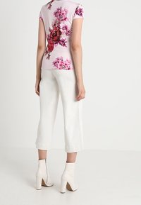 Top rosa de manga corta con estampado floral, pantalones blancos cortos y botas de tobillo color crema. Tejido texturizado y diseño ajustado.