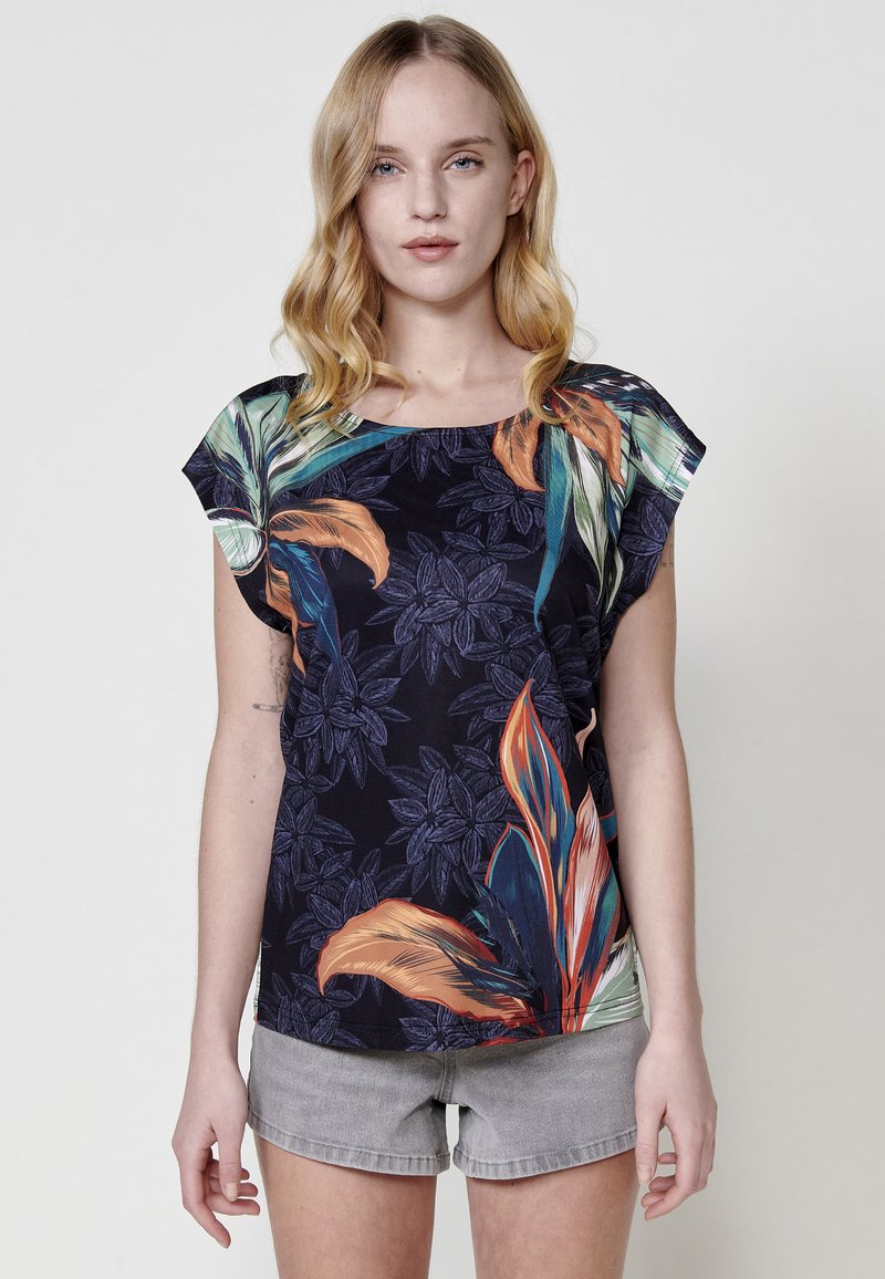 Top à imprimé floral avec des manches courtes, affichant un fond sombre et des feuilles colorées vives. Le matériau semble doux avec une coupe décontractée.