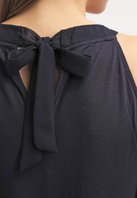 Top sin mangas de color navy con un corte en la espalda en forma de llave y cierre de lazo, fabricado con una tela suave de textura lisa y costuras limpias.