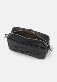 Borsa a pochette in pelle nera con superficie testa di moro, chiusura con zip e logo impresso. Internamente rivestita con un colore a contrasto. Forma rettangolare.