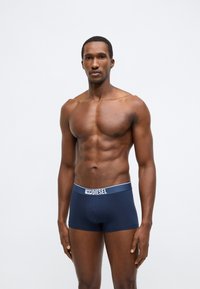 Pantalones bóxer azul marino con una cintura blanca que lleva el logo "DIESEL", fabricados con una tela suave y elástica. Textura lisa, diseño ajustado.