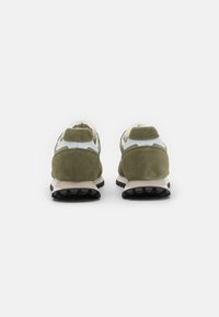 Zapatillas de ante verdes con un diseño en blanco y gris, que presentan una forma redondeada, una parte superior texturizada y una suela de goma negra.