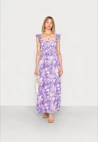 Vestido longo floral roxo com alças com babados, decote quadrado e cintura ajustada. Usado com saltos laranjas e uma bolsa neutra.