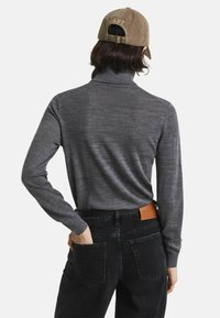 Grijze coltrui met lange mouwen, gemaakt van zacht materiaal. Gecombineerd met zwarte denim jeans met een leren label op de achterkant.