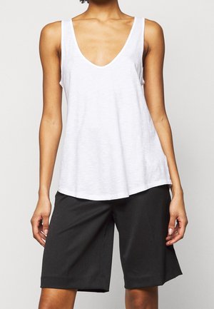 White sleeveless top with a deep V-neck, made of lightweight fabric. Paired with loose-fitting black shorts. Simple and minimal design.
