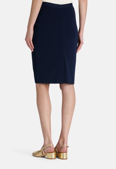 Tamsiai mėlynas pieštuko sijonas su elegantišku dizainu ir nugaroje esančia skeltimi. Pora su auksinėmis pintinėmis slingback bateliais, turinčiais storą kulną.
