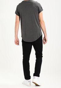 Šedá košile s krátkým rukávem a zaobleným lemem, v kombinaci s černými slim-fit kalhotami a bílými teniskami, pohled zezadu.