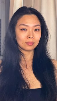 Persona con cabello largo y lacio negro, piel clara y maquillaje mínimo. Lleva una blusa negra con un delicado collar, con un fondo neutro.