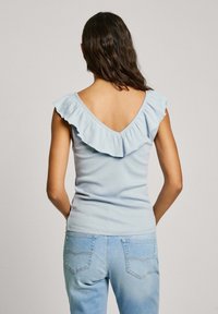 Hellblaues geripptes Tanktop mit V-Ausschnitt und Rüscheträgern. Trägt dazu hellblaue enganliegende Jeans mit Gesäßtaschen.